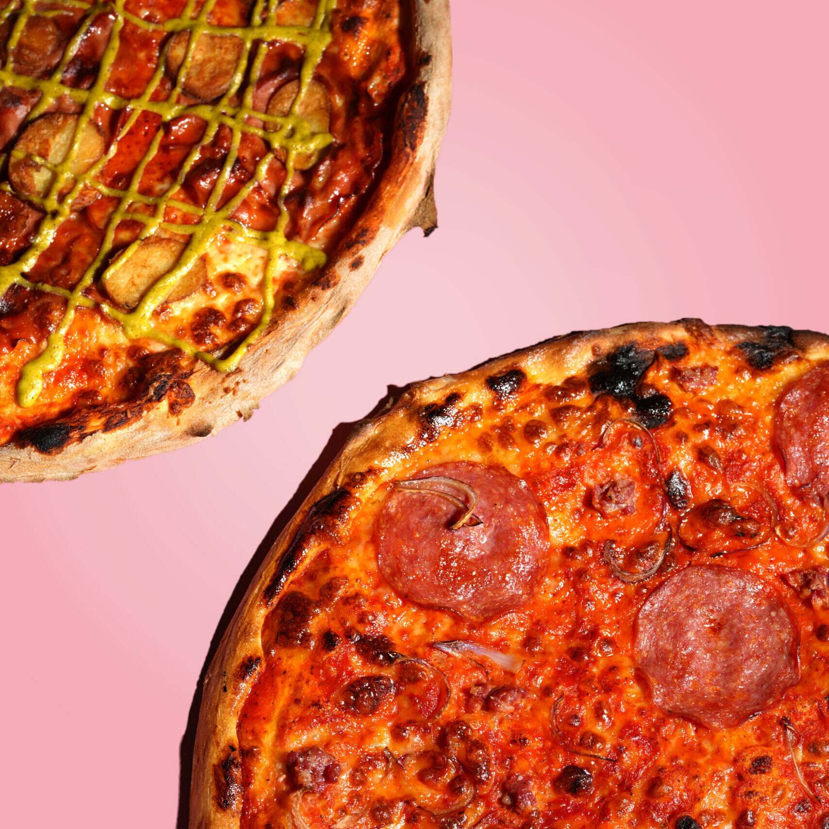20 inch pepperoni pizza and mortadella pizza on a pink background