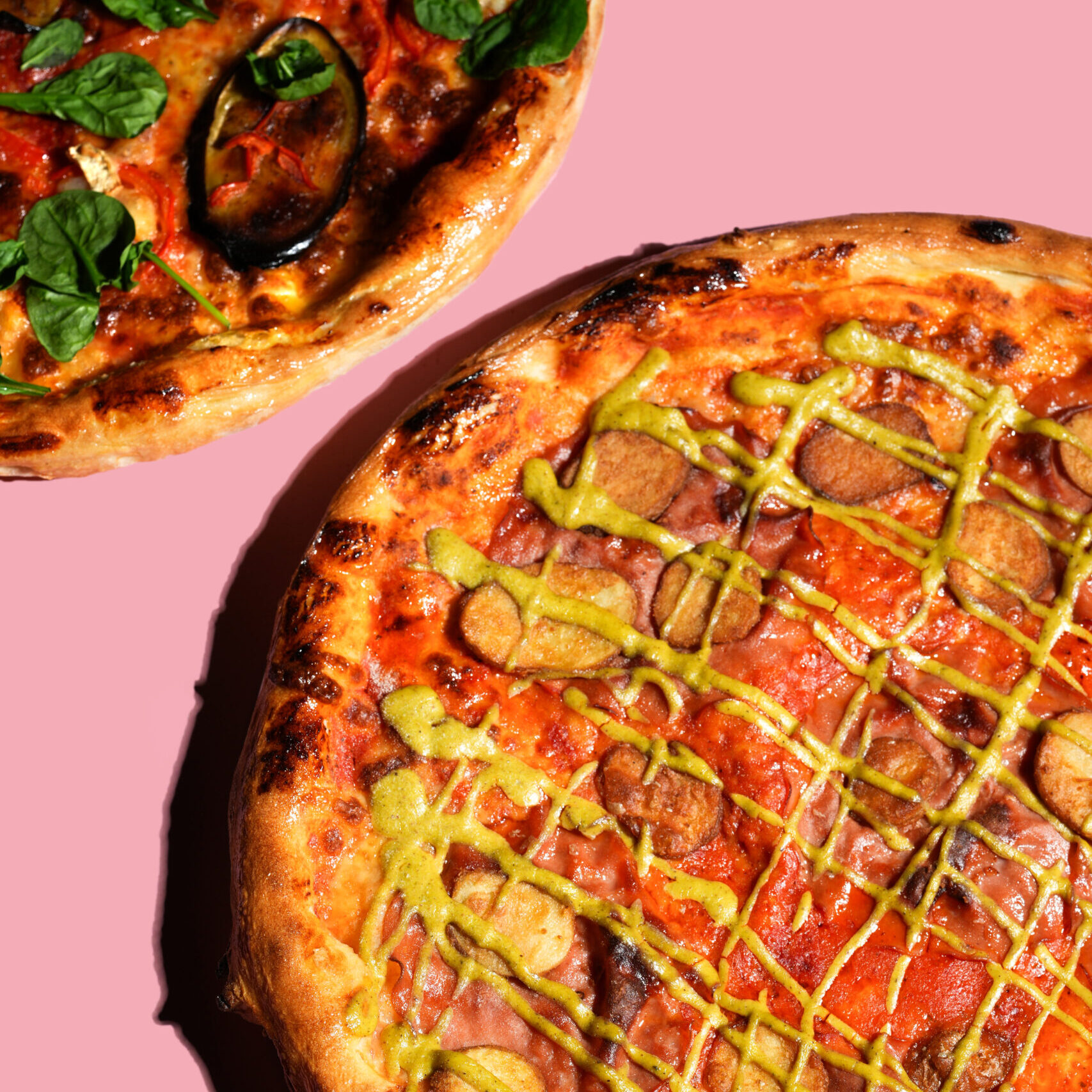 20 inch aubergine pizza and mortadella pizza on a pink background