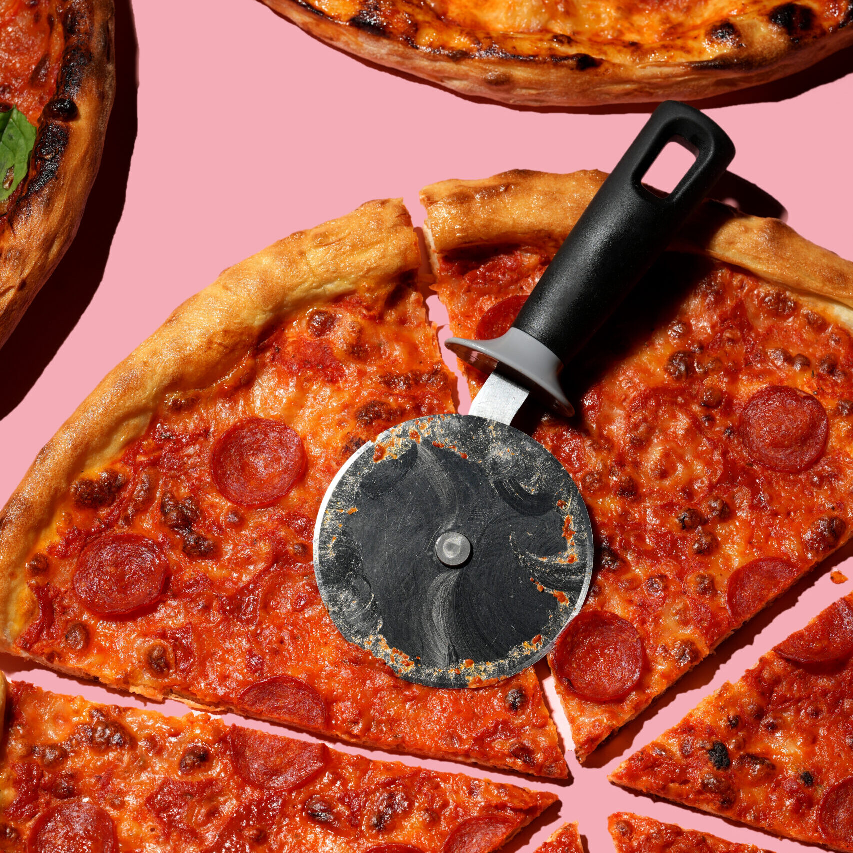 20 inch pepperoni pizza with a pizza slicer on a pink background