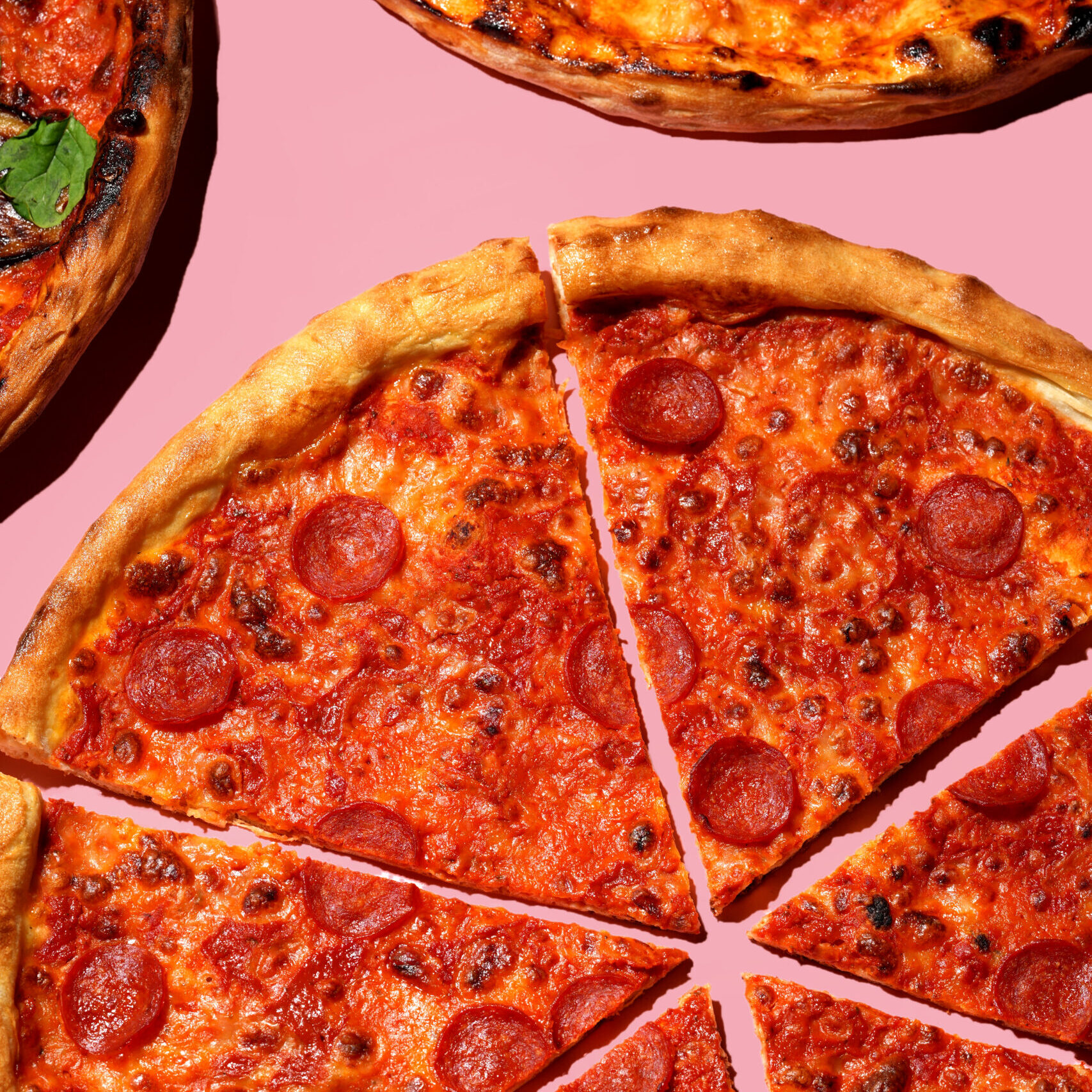 20 inch pepperoni pizza cut into slices on a pink background