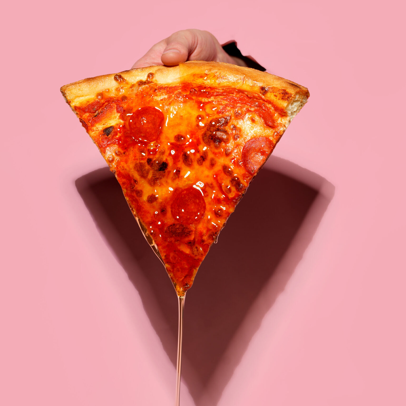 hand holding a slice of pepperoni pizza dripping in hot honey sauce
