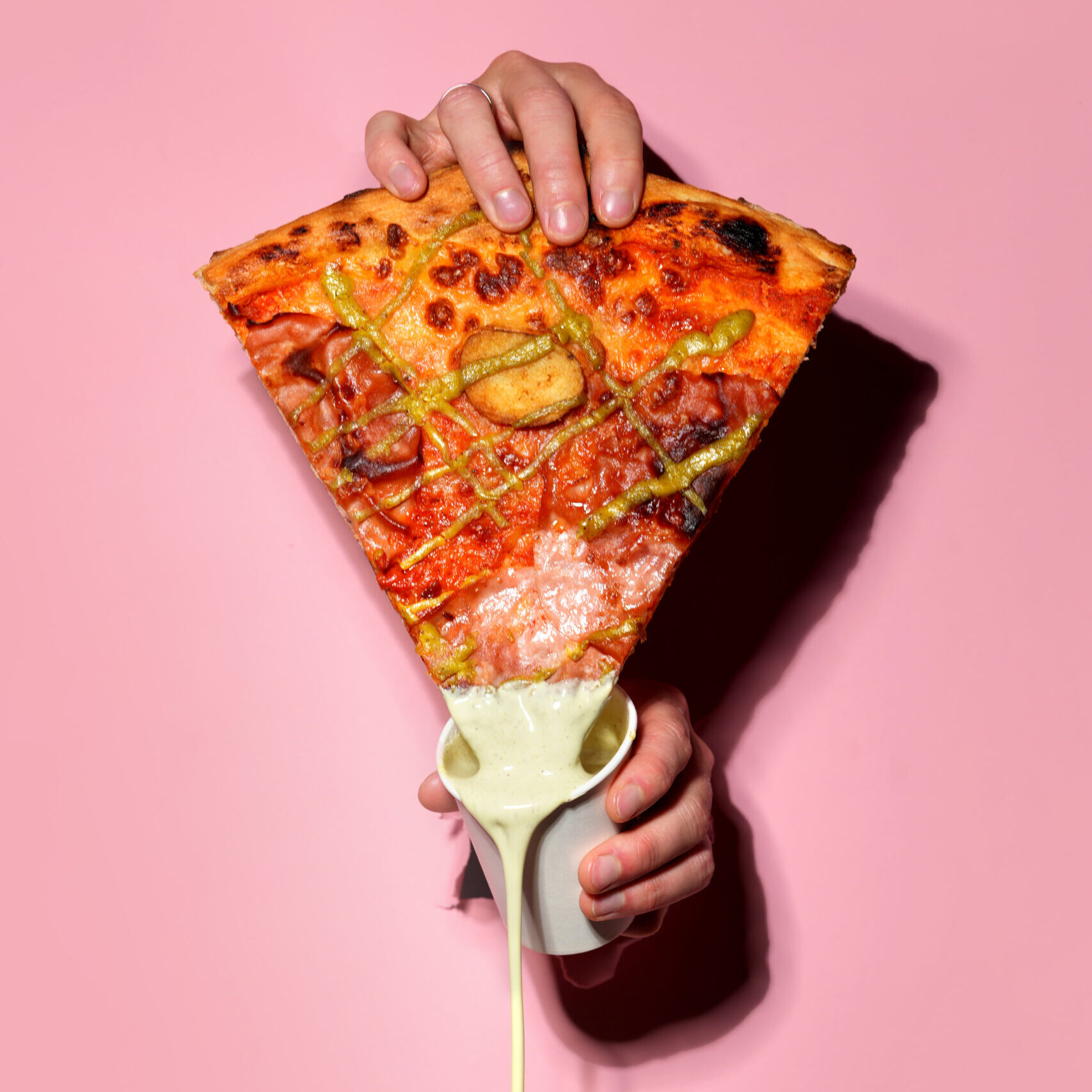hand holding a slice of Mortadella pizza dipped in Garlic aioli sauce